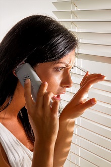 a young woman watching something through the blinds of her windo