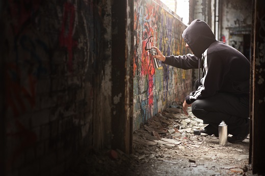 Illegal Young Man Spraying Black Paint On A Graffiti Wall.